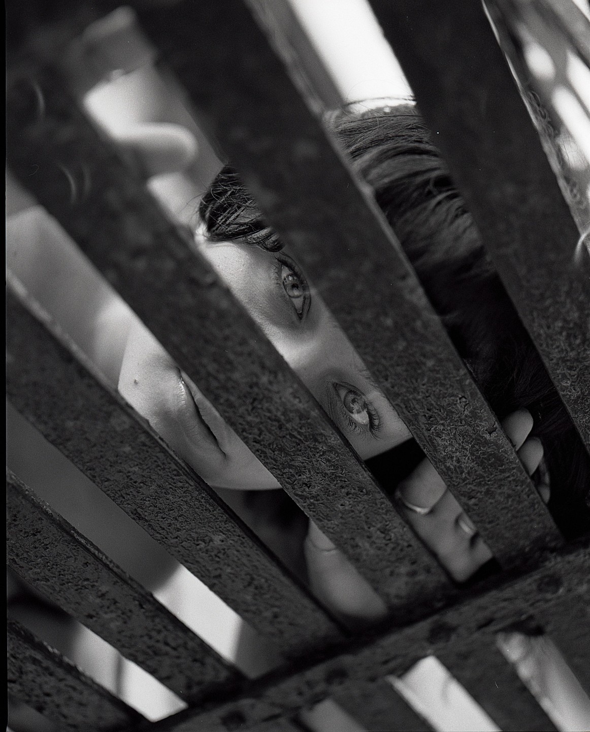 A woman's face is visible through a rusty metal grate.