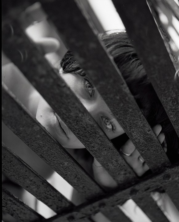 A woman's face is visible through a rusty metal grate.