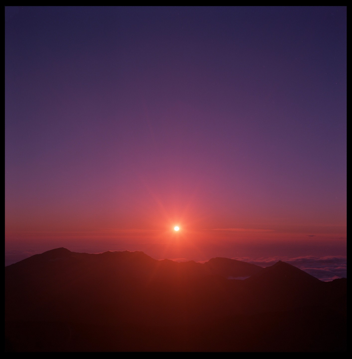 The sun rises over a mountain range, casting a red and purple glow across the sky.