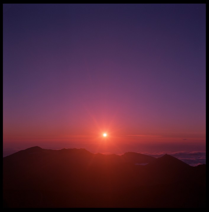 The sun rises over a mountain range, casting a red and purple glow across the sky.