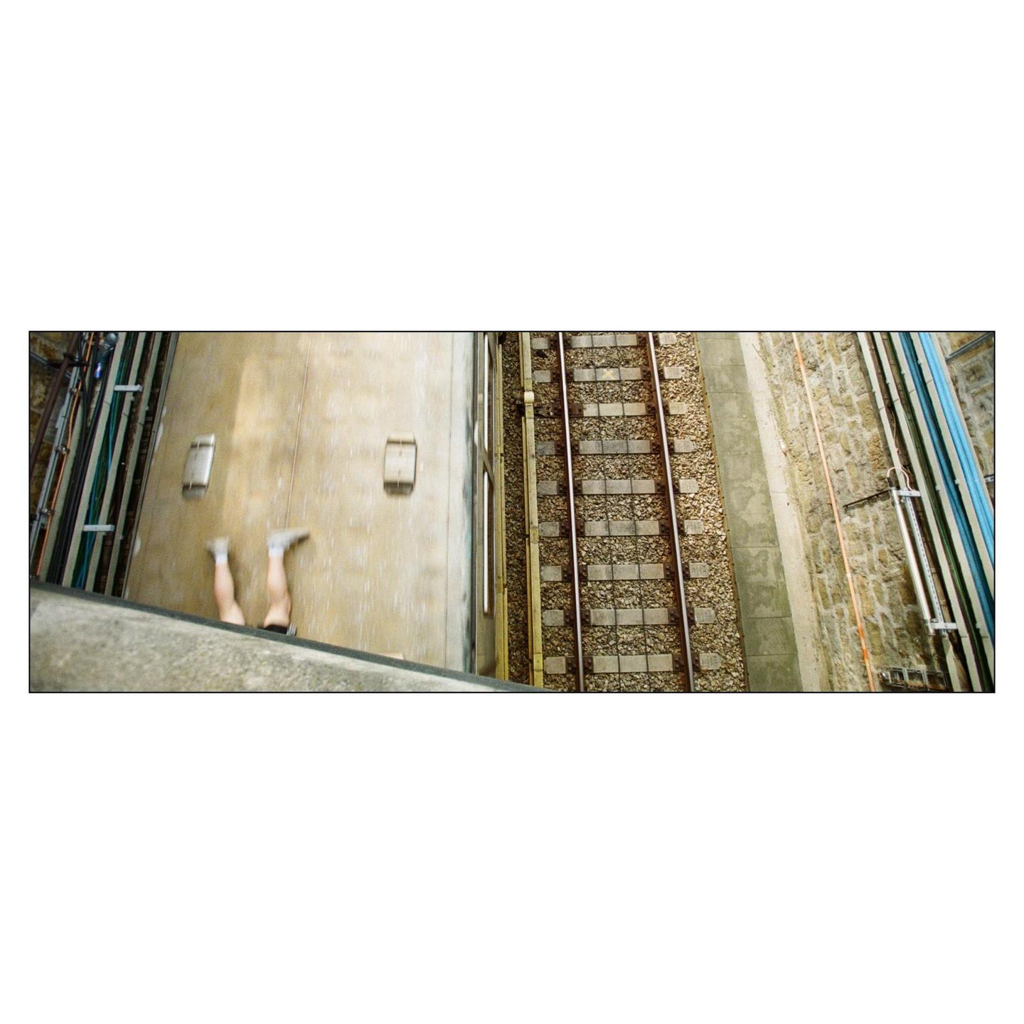 A person's legs are visible on the roof of a train next to train tracks.