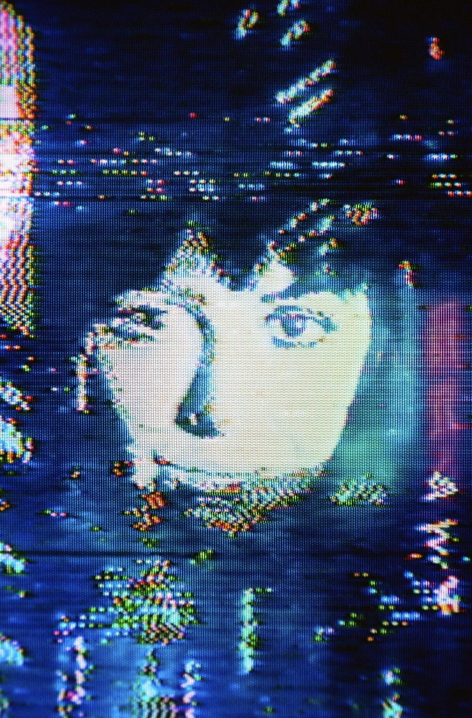 A woman's face is visible through a heavily glitched and pixelated screen.