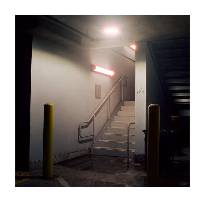 A concrete stairwell with a metal railing is illuminated by fluorescent lights, with two yellow bollards in the foreground.