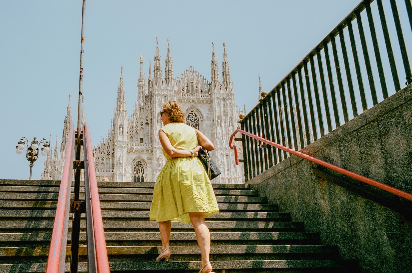 A woman in a yellow dress walks up a stone staircase with a large gothic cathedral in the background.