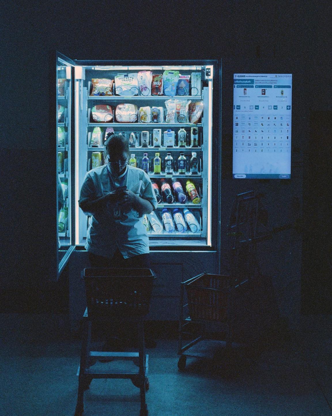 A person stands in front of a brightly lit vending machine, with two shopping carts nearby.