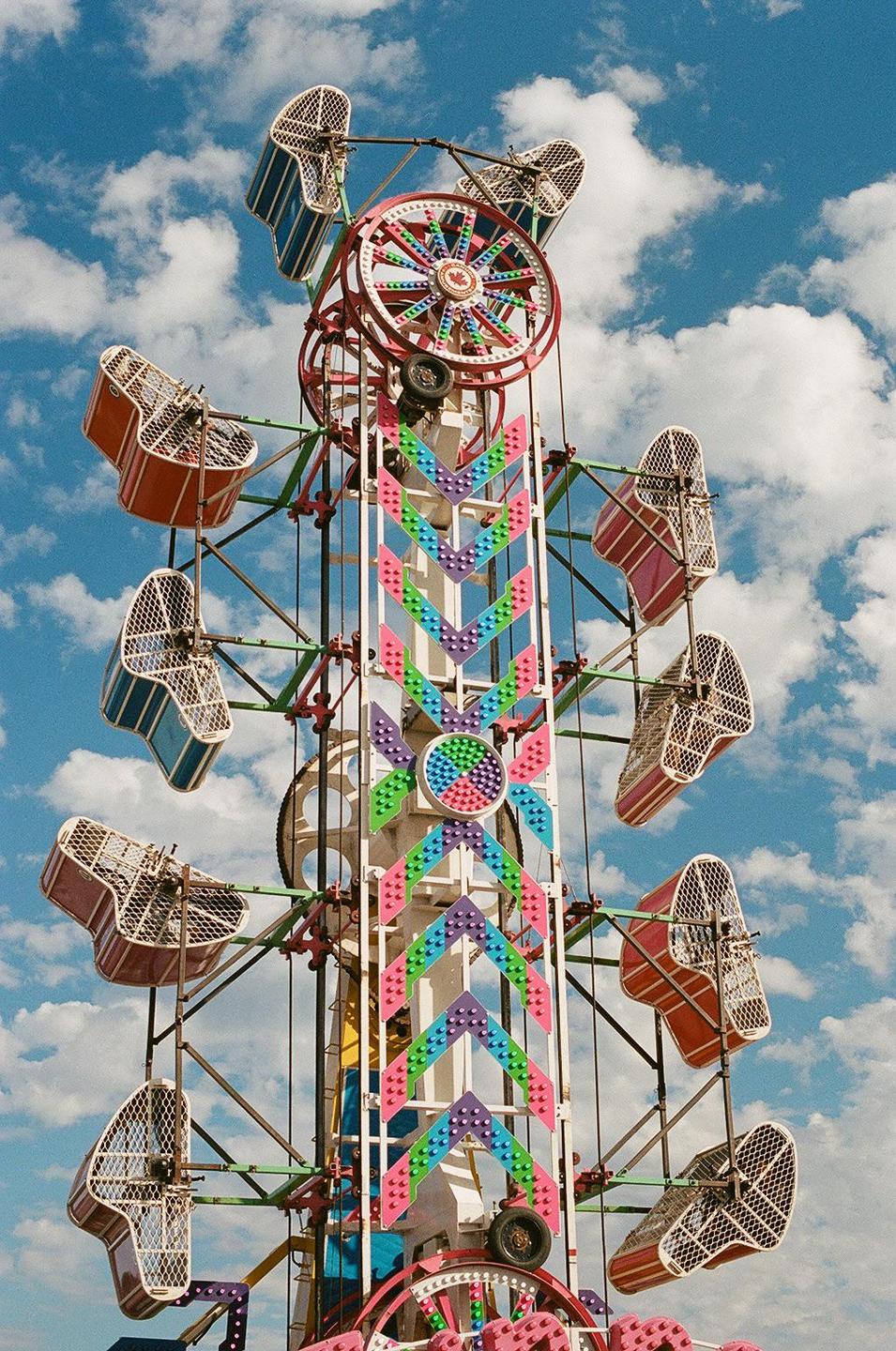 A colorful carnival ride with multiple passenger cages is set against a bright blue sky with white clouds.