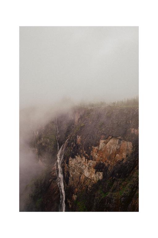 A waterfall cascades down a rocky cliff face shrouded in mist.