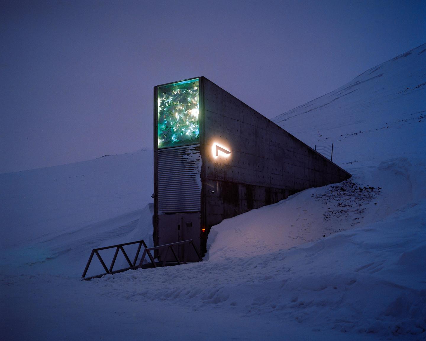 The Global Seed Vault is illuminated at night, surrounded by snow-covered mountains.