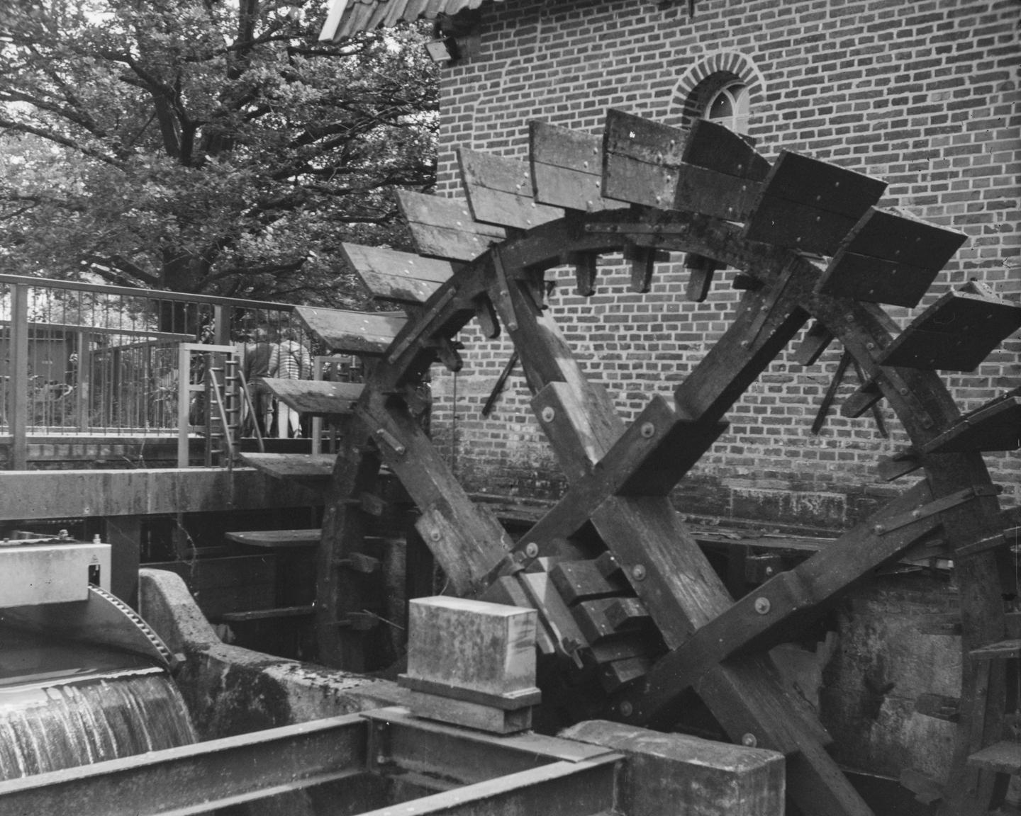A large wooden waterwheel is next to a brick building with a small arched window.