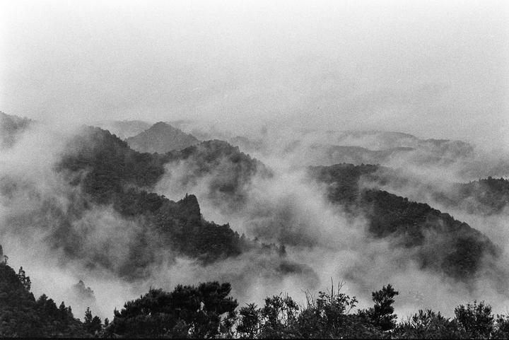 A black and white landscape shows a mountain range covered in fog.