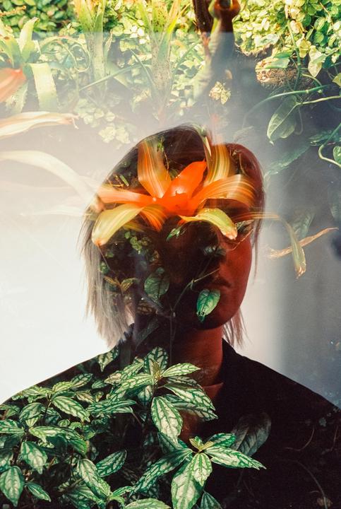 A double exposure shows a woman's head overlaid with a vibrant orange flower and various green plants.