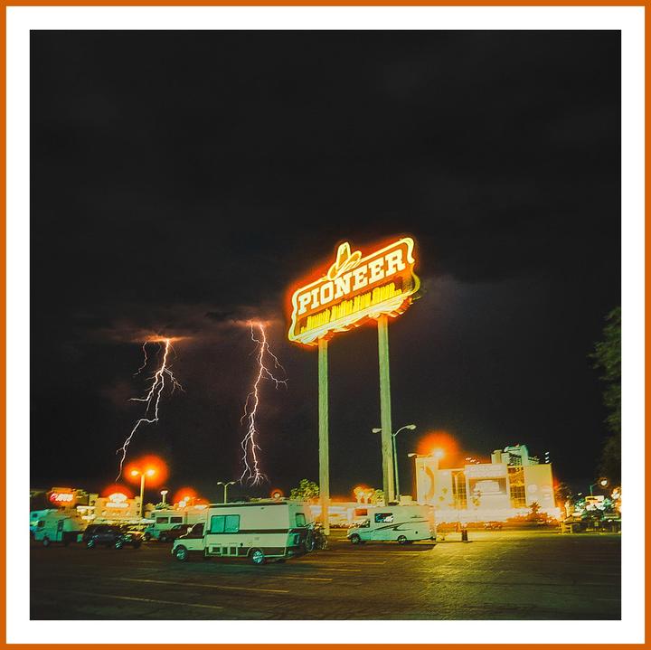 Lightning strikes behind a neon "Pioneer" sign in a parking lot at night.