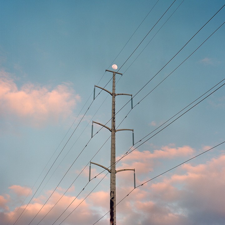 A full moon is visible above a power line against a blue sky with pink clouds.