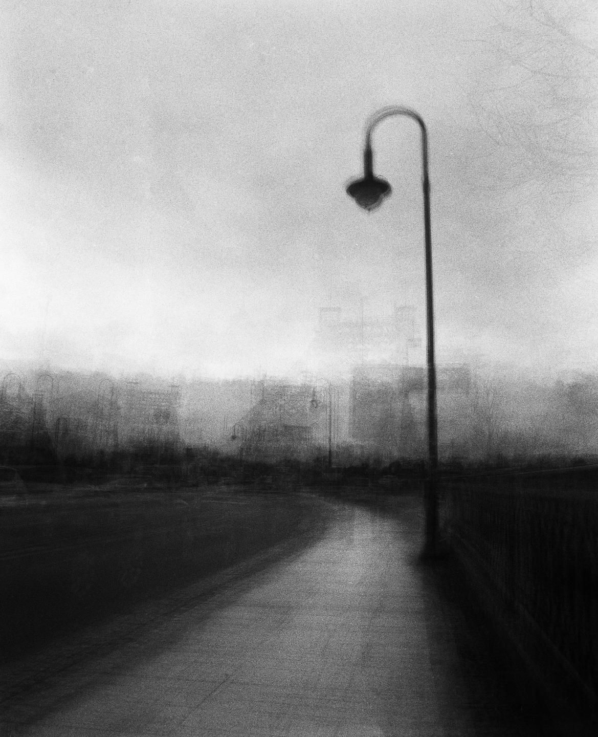 A street lamp stands beside a path with a blurry cityscape in the background.