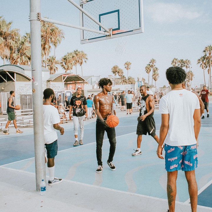 Several men play basketball on an outdoor court lined with palm trees.