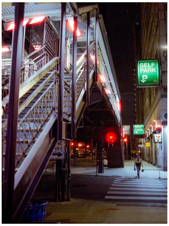A person walks across a crosswalk at night next to a large metal structure and a "self park" sign.