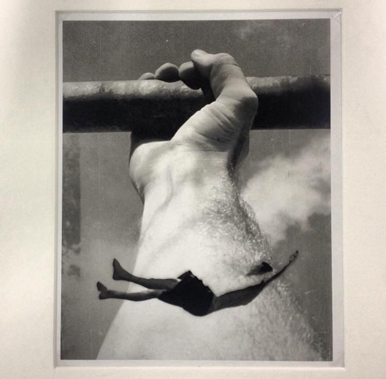 A large hand holds onto a bar while a small figure falls through the air below.