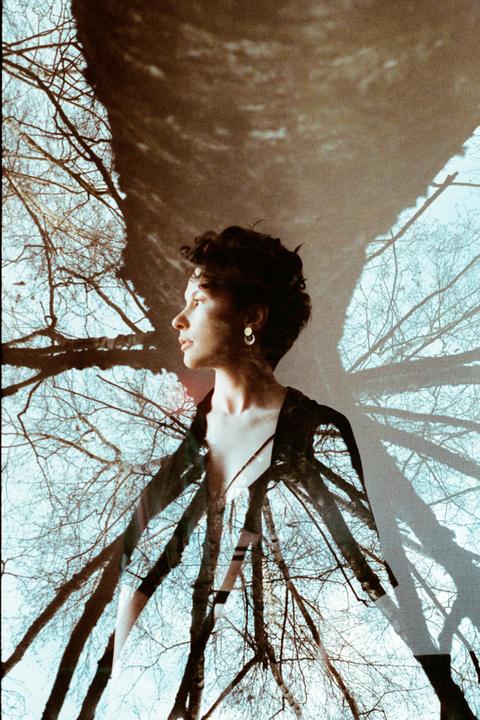 A woman's profile is superimposed over a background of bare tree branches against a light blue sky.