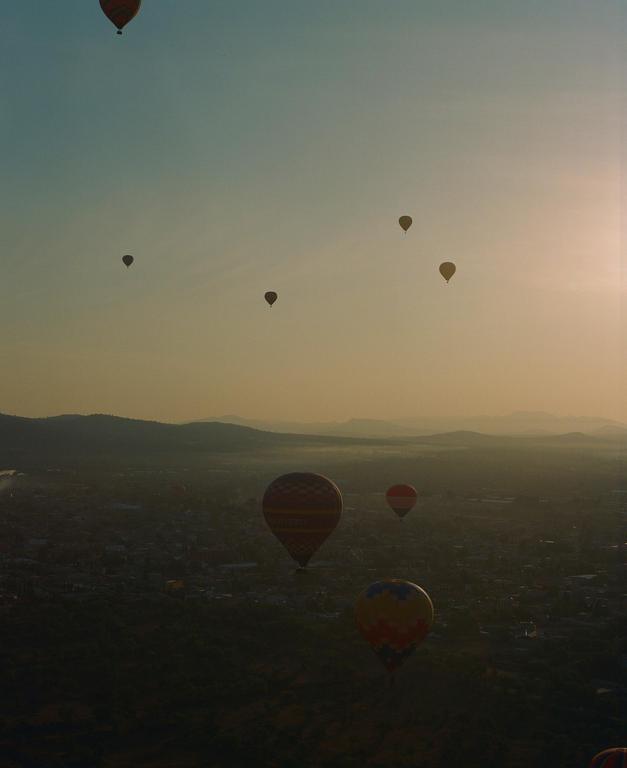 Hot air balloons float above a city at dusk with mountains in the distance.