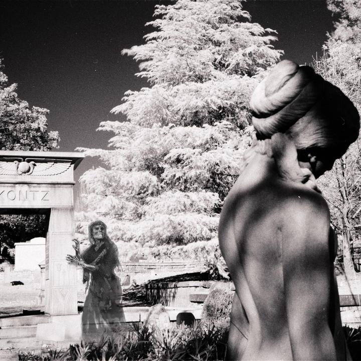A ghost-like figure stands in front of a tombstone with a statue in the foreground.