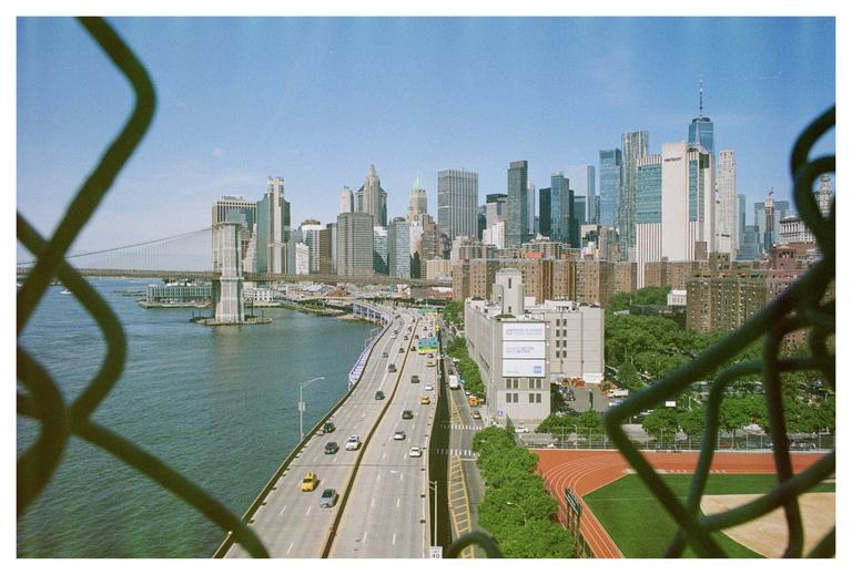 A city skyline with a bridge and a highway is seen through a chain-link fence.