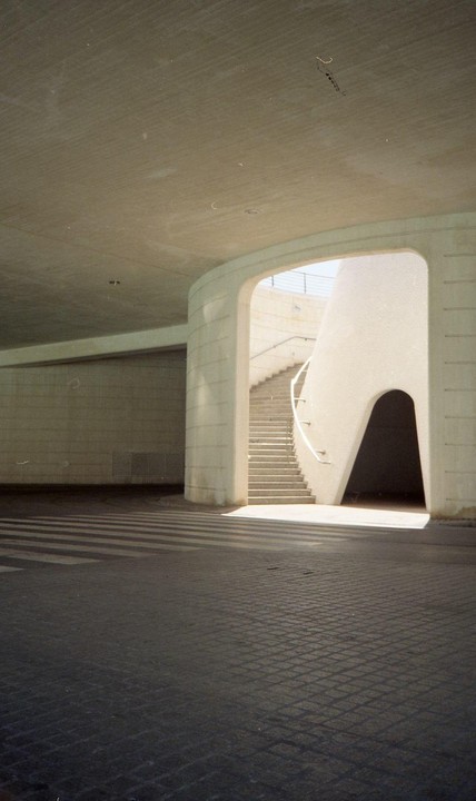 Sunlight casts shadows on the ground and illuminates a concrete staircase leading up from an underpass.