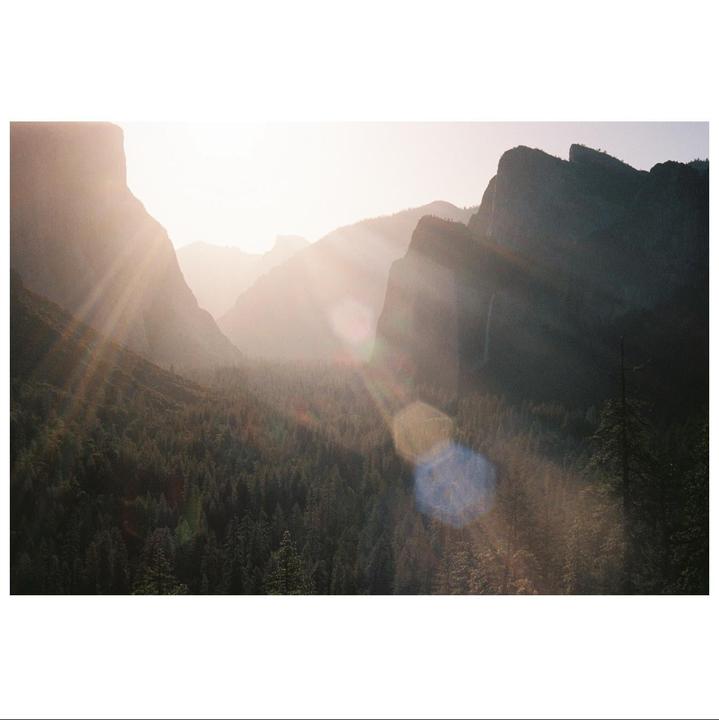 Sunlight streams over a valley filled with trees and surrounded by mountains.