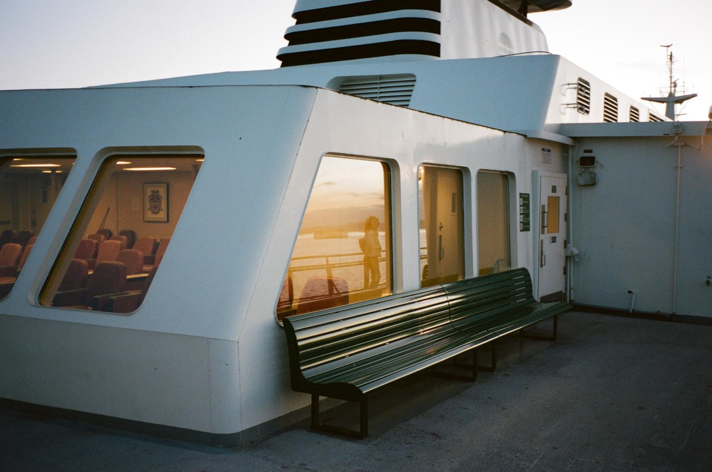 A white ferry with a green bench on its deck reflects the golden hour light on its windows.