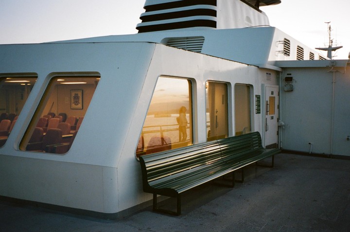 A white ferry with a green bench on its deck reflects the golden hour light on its windows.