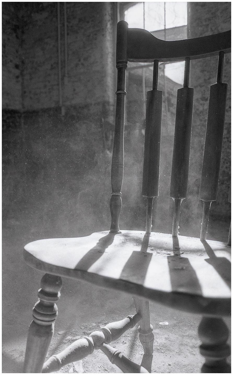 Sunlight streams through a window, illuminating dust motes and casting shadows from a wooden chair.