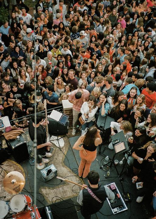 A large crowd of people watches a band perform on a stage.
