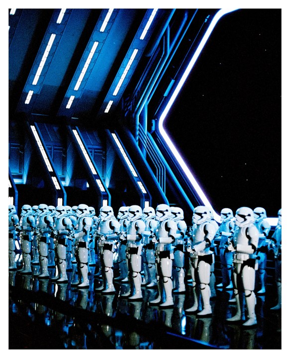 A large group of stormtroopers stand in formation in a hangar with blue neon lights.