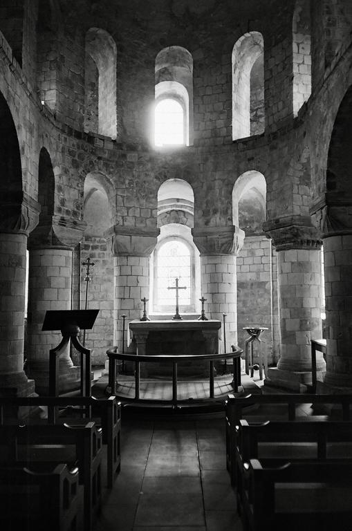 A stone church interior with an altar and cross is illuminated by light from a window.
