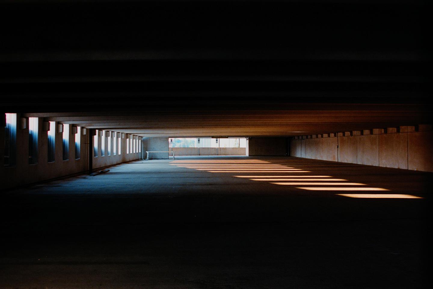 Sunlight streams through openings in a parking garage, creating long shadows on the floor.