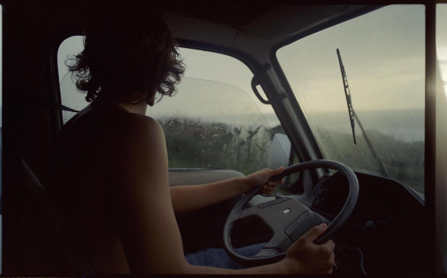 A person with curly hair drives a vehicle with a wet windshield.