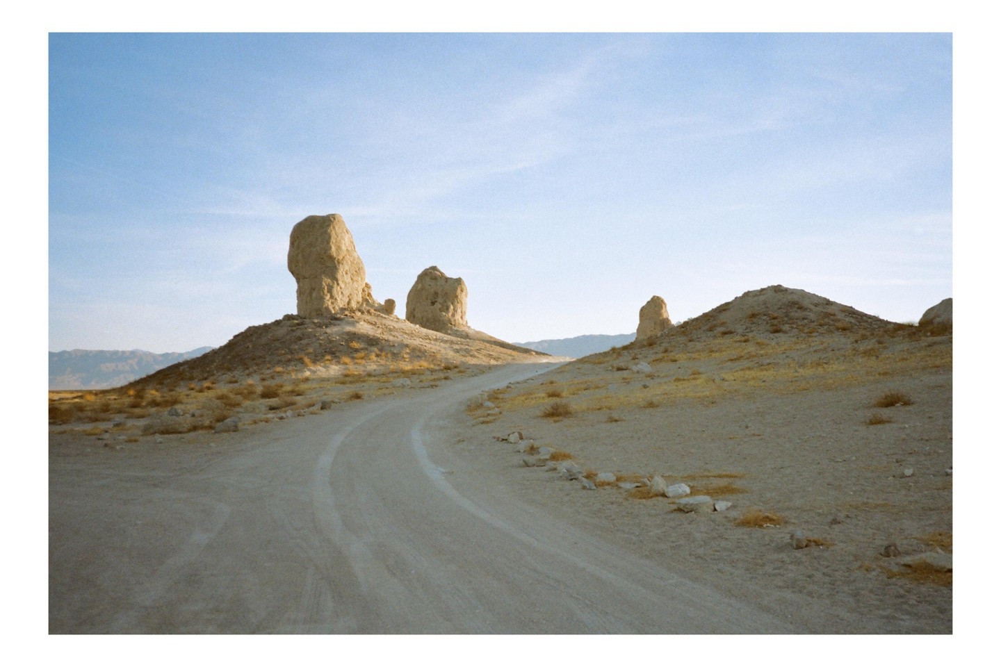 A dirt road curves through a desert landscape with several large rock formations under a clear sky.