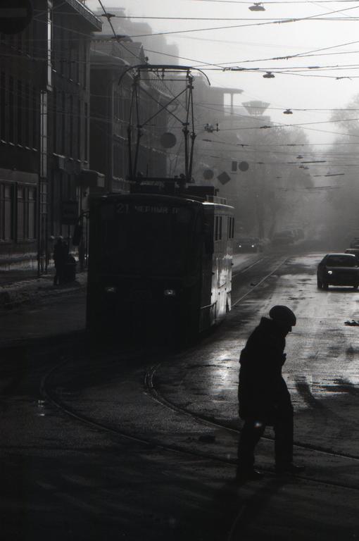 A person walks on a wet street next to a tram on a hazy day.