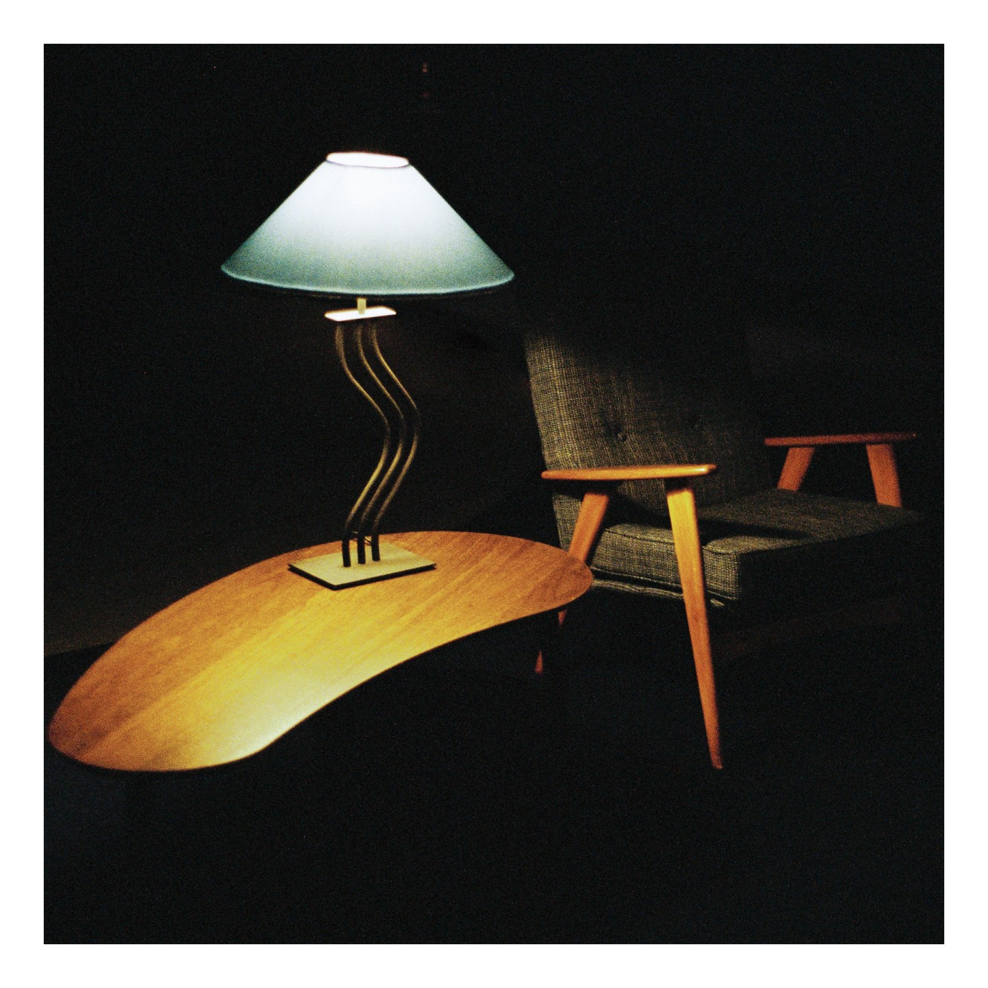 A lamp with a light blue shade sits on a kidney-shaped table next to an armchair.
