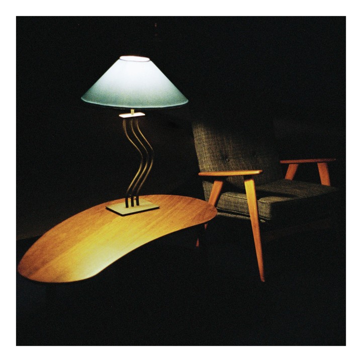 A lamp with a light blue shade sits on a kidney-shaped table next to an armchair.