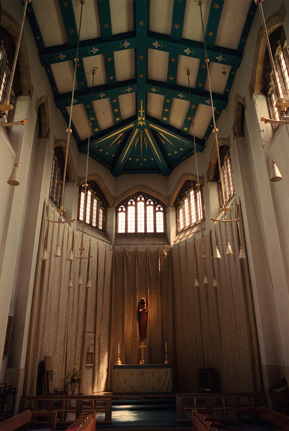 The interior of a cathedral features a high, decorated ceiling, stained glass windows, and an altar with a statue.