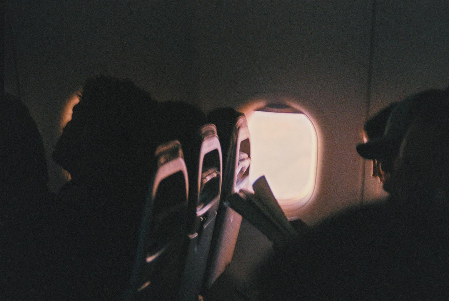 The interior of an airplane cabin is visible with passengers silhouetted against a bright window.