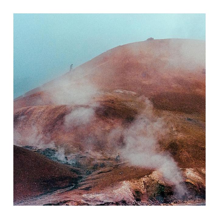 A person stands on a barren, steaming hillside under a hazy sky.
