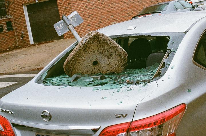 A concrete block and a street sign have fallen through the rear window of a silver car, shattering the glass.