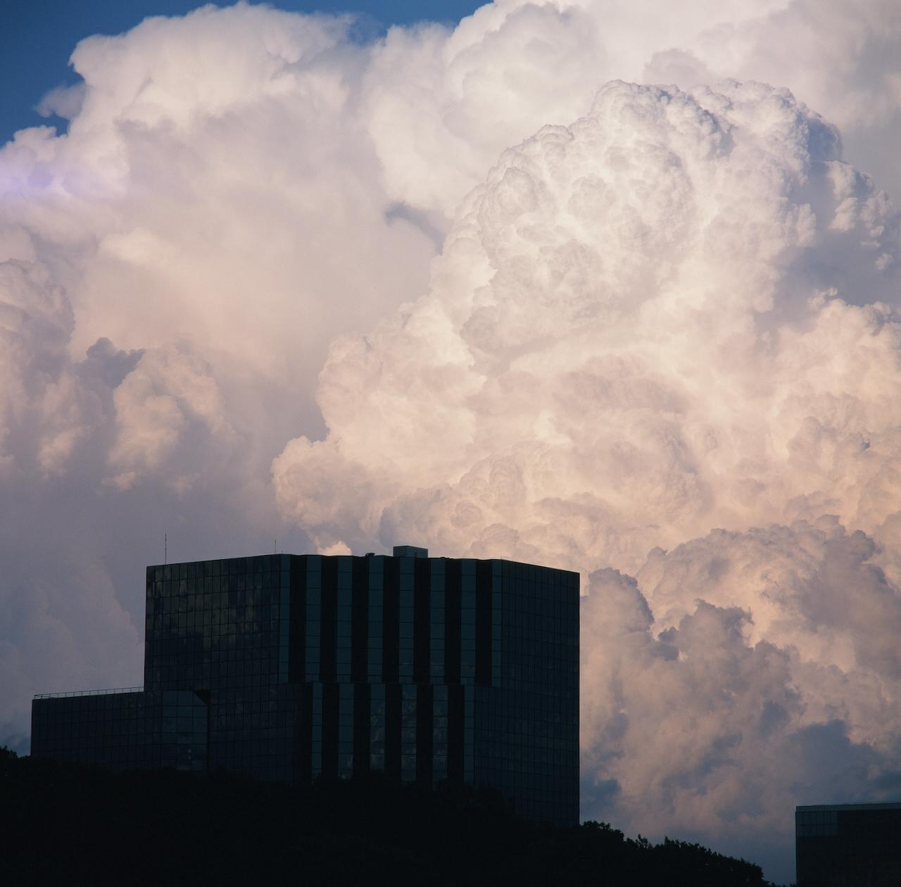 A dark building is silhouetted against a dramatic sky filled with large, fluffy clouds.