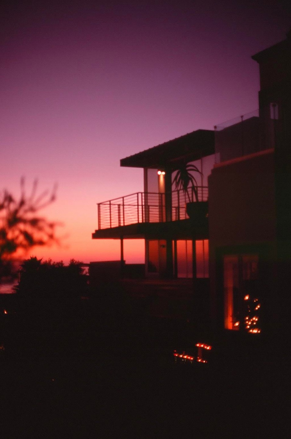 A modern house with a balcony is silhouetted against a vibrant purple and orange sunset.