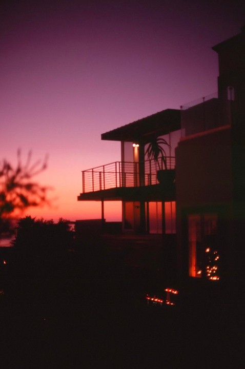 A modern house with a balcony is silhouetted against a vibrant purple and orange sunset.