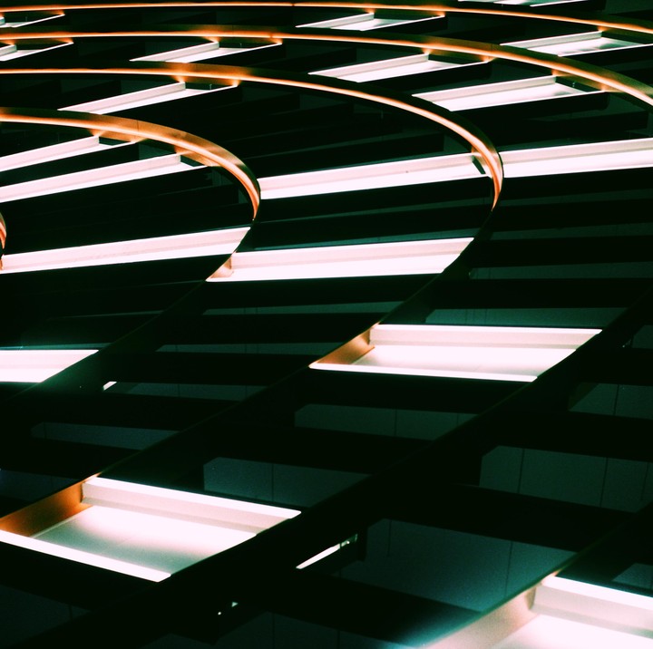 A pattern of illuminated rectangular lights and curved orange beams creates an abstract composition.