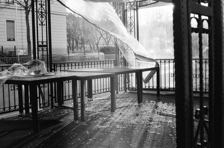 A plastic sheet blows over tables on a balcony with a street and building in the background.