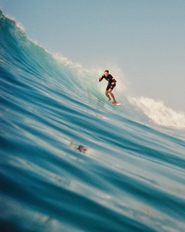 A surfer in a wetsuit rides a large blue wave.