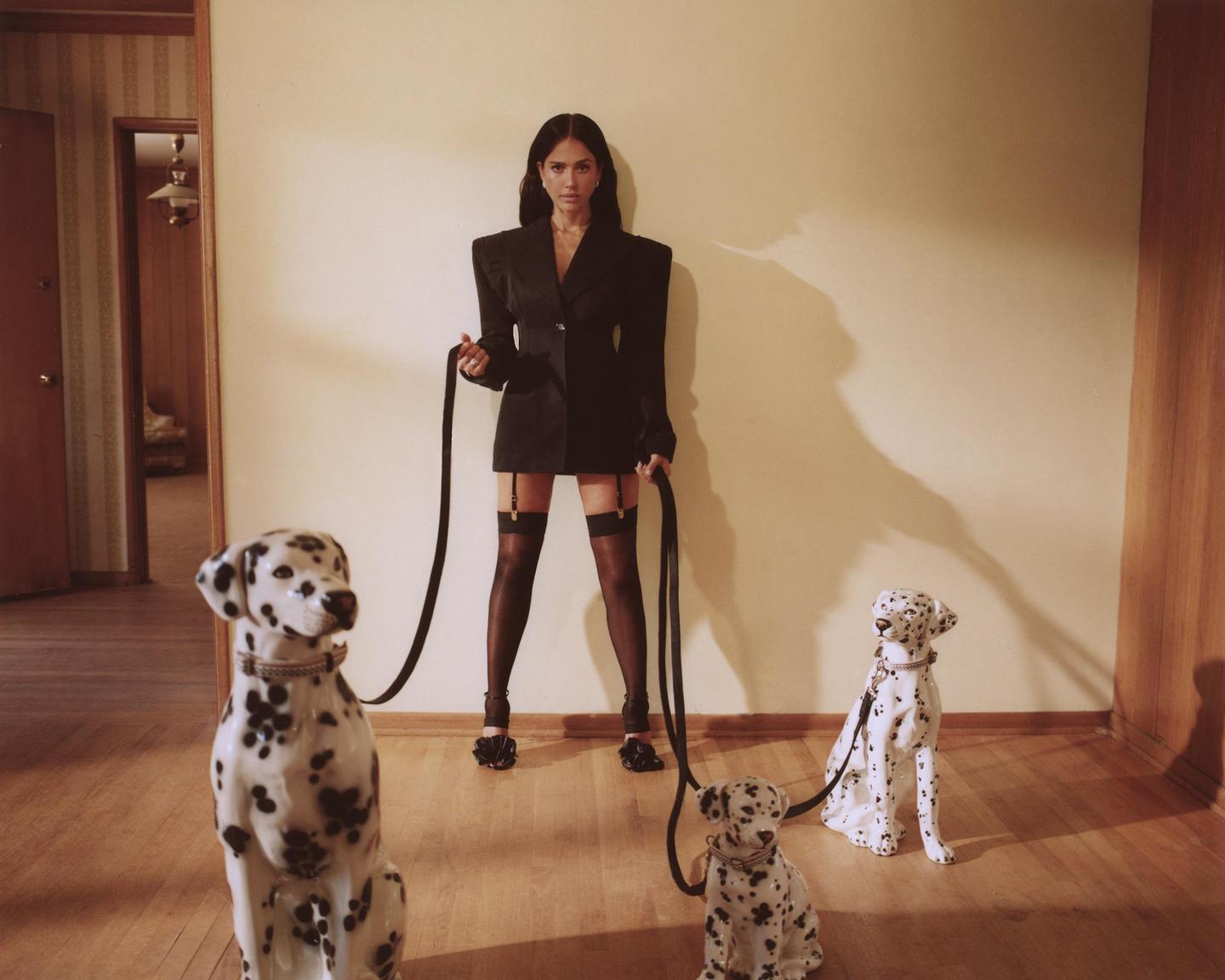 A woman in a blazer and stockings holds leashes attached to three dalmatian statues.
